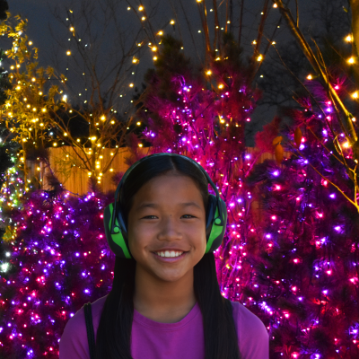 Girl with noise canceling headphones in front of holiday trees